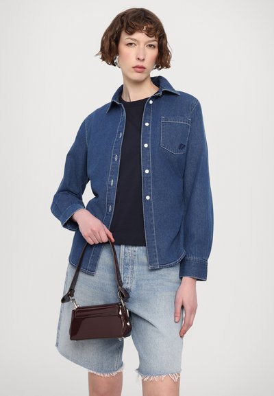 Chemise en denim bleu moyen avec fermeture à boutons, poche poitrine et manches retroussées, associée à un short en denim bleu clair effiloché et un sac à main bordeaux.