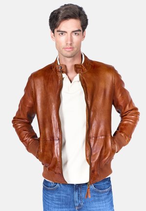 Giacca bomber in pelle marrone con colletto alto, chiusura a zip, tasche laterali e polsini a costine. Texture liscia con un leggero lucido.