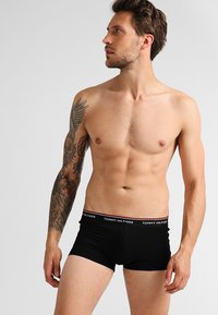 Sorte bomulls boxer briefs med en merkebrandet midje, som har en tett passform og glatt tekstur, båret av en skjorteløs mannlig modell.