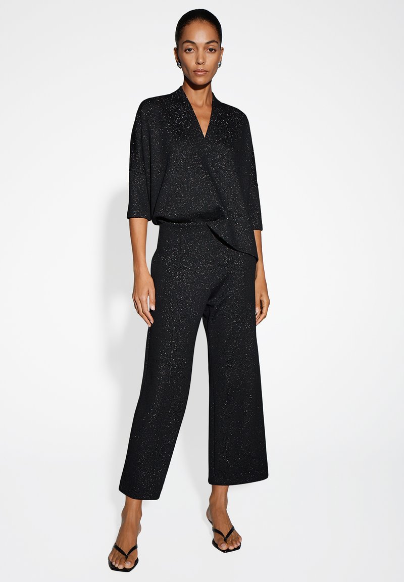 Zwart outfit met een losse, korte mouwen top en wijde broek, beide met glinsterende accenten voor een textuur uitstraling.