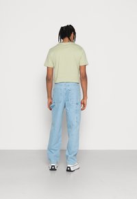 Vaaleanvihreä puuvillainen t-paita pyöreällä kaula-aukolla, jonka kanssa on yhdistetty vaaleansiniset farkku cargo-housut, joissa on sivutaskut ja rento istuvuus.