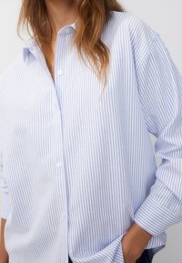 Lichtblauwe en witte gestreepte blouse met een losse pasvorm, knoopsluiting aan de voorkant, klassieke kraag en opgerolde lange mouwen, gemaakt van een zachte stof.