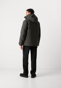 Giacca imbottita grigio scuro con cappuccio, caratterizzata da una vestibilità dritta e un design minimalista. Abbinata a pantaloni neri a gamba larga e scarpe voluminose.