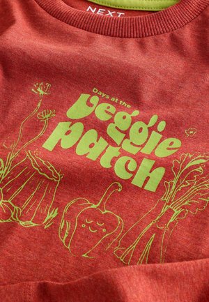 Sweatshirt en coton rouge avec un col côtelé. Présente un texte graphique vert et des illustrations de légumes dans un design ludique.