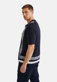 Navy short-sleeve knit cardigan with white striped detailing along the front and hem, featuring a round neckline and button closure.