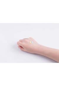 Två små rektangulära bitar i guld och ljusblått som vilar på en hand med ljus hudton mot en enfärgad vit bakgrund.