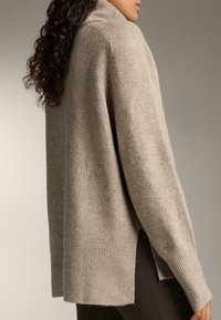 Pulover tricotat de culoare bej deschis, cu guler înalt, manșete cu nervuri și slituri laterale. Textură moale și croială lejeră.