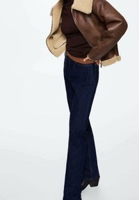 Brązowa skórzana kurtka z kołnierzem z owczej wełny, ciemnoniebieskie dżinsy dzwony i czarne botki na obcasie. Ciemna paleta kolorów, casualowy styl, dopasowany krój.