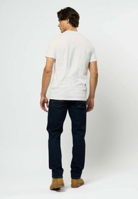 Balta trumpa rankovėmis marškinėliai derinami su tamsiai mėlynomis džinsais ir šviesiai rudos spalvos botais. Marškiniai turi apvalų iškirpimą, prigludusį siluetą ir lygų paviršių.