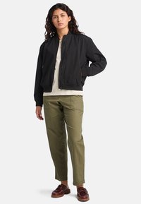 Black bomber jacket with ribbed cuffs and collar, paired with olive green pants and brown leather shoes. Simple design, no visible patterns.