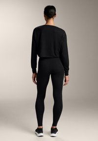 Crni dugi rukavi uski top i crne tajice, napravljeni od glatkog materijala, pripijenog kroja i minimalističkog dizajna, uparen s crnim sportskim cipelama.