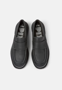 Svarta läder slip-on skor med rund tå och texturerad gummisula. Har ett platt band över fotryggen. Inuti finns ett kontrasterande mönster.