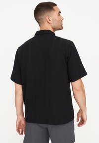 Maglietta nera a maniche corte con un motivo tessuto a trama, colletto ripiegato e vestibilità morbida. Il retro presenta un orlo dritto.