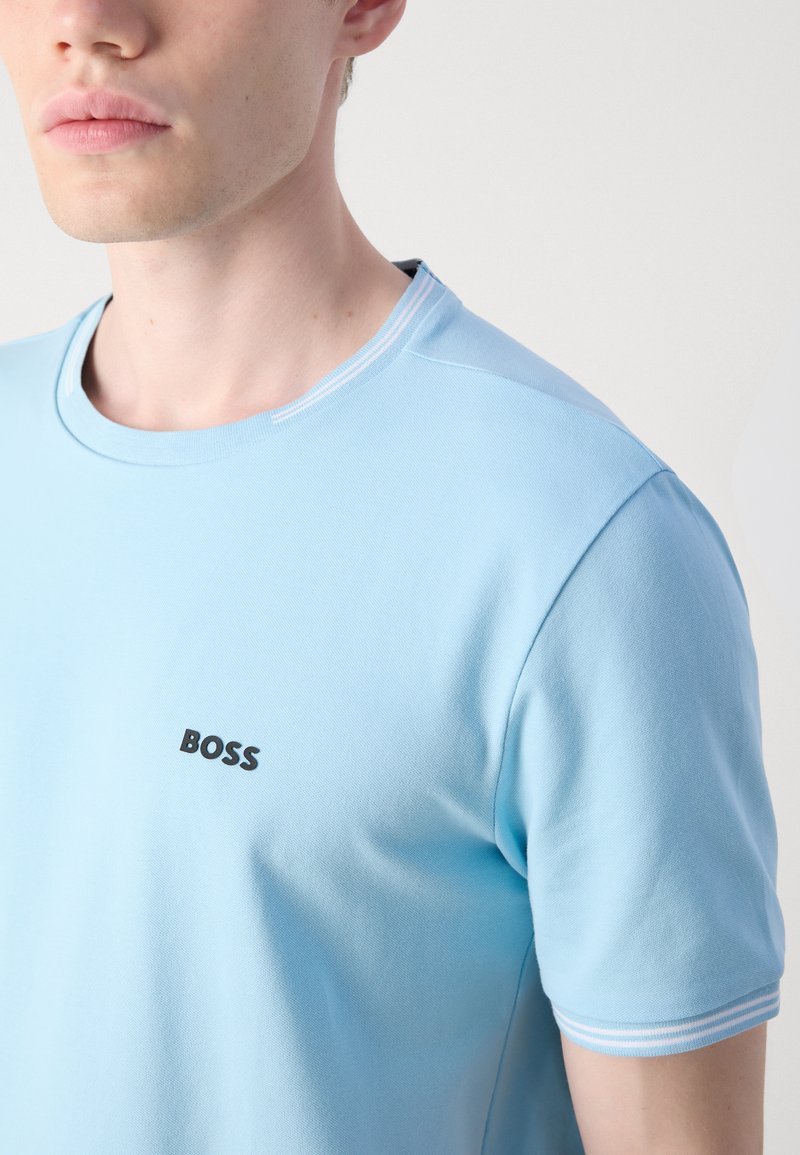 T-shirt bleu clair à col rond en coton, avec des manches courtes et un logo "BOSS" noir sur la poitrine ; détail de col fin côtelé.