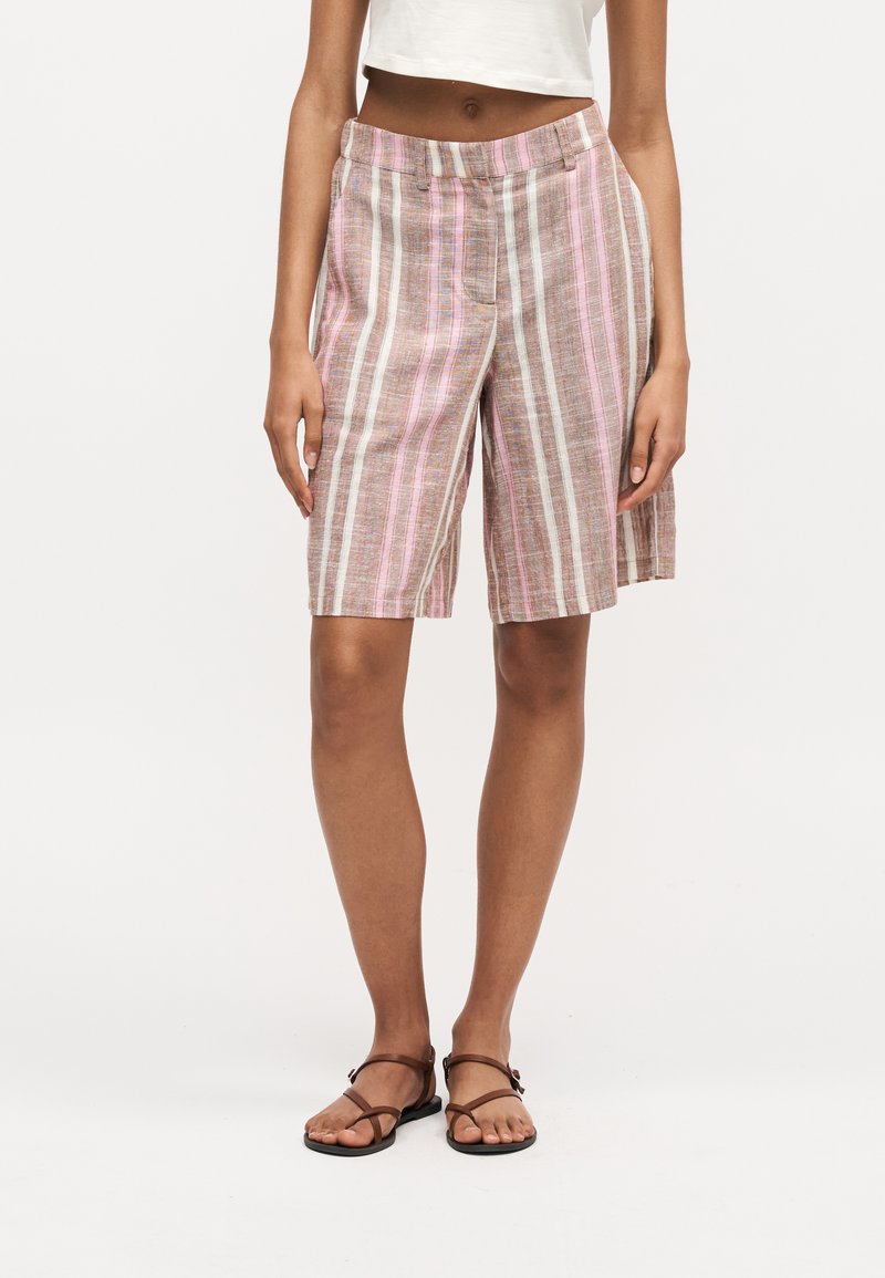 Femme portant un short mi-long à rayures verticales roses, marron et blanches, un top court blanc et des sandales marron à brides.