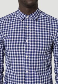 Blå och vit rutad skjorta med knappkläppskrage, långa ärmar och bröstficka. Tillverkad av lätt tyg med en slät textur.