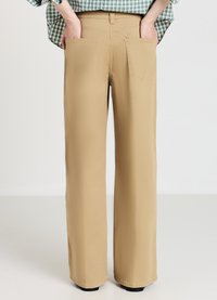 Pantalon beige à jambes larges avec poches arrière, confectionné dans un tissu doux, doté d'une texture lisse et d'une finition nette à l'ourlet.