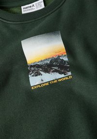 Roheline spordipusa, millel on mäe graafika päikeseloojangu taustal, ja allpool teksti "AVASTA MAAILM" kollases kirjas.