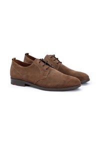 Des chaussures en cuir suédé marron à lacets, avec une texture lisse, un bout arrondi et une semelle en caoutchouc plate. Elles présentent des coutures minimales et des lacets foncés.