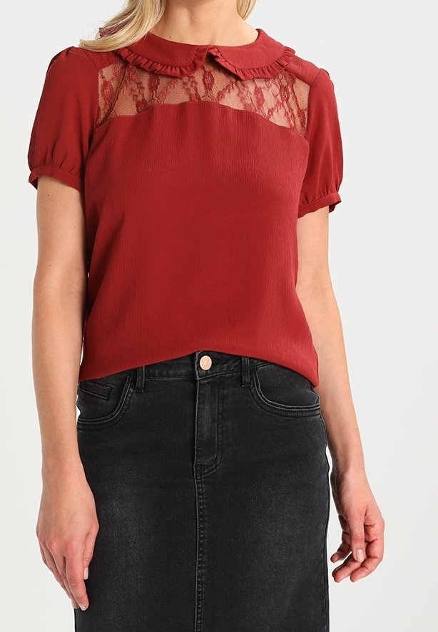 Blouse rouge avec yoke en dentelle, col à volants et manches courtes bouffantes, associée à une jupe en denim noire. Texture lisse.