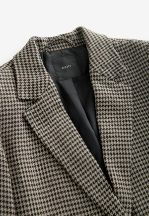 Sacou cu model houndstooth în bej și negru, având guler ascuțit și căptușeală interioară neagră; materialul pare texturat.