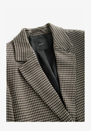 Houndstooth-patterned blazer in beige and black, featuring a notched collar and black interior lining; fabric appears textured.