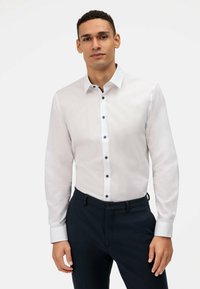 Witte lange mouwen shirt met donkere knopen, een button-down kraag en een effen textuur, gecombineerd met donkere gepashionneerde broeken.