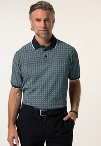 Pánská polokošile s krátkým rukávem v námořnické modři s geometrickým vzorem, bílými akcenty na límci a volným střihem, ve spojení s tmavými kalhotami.