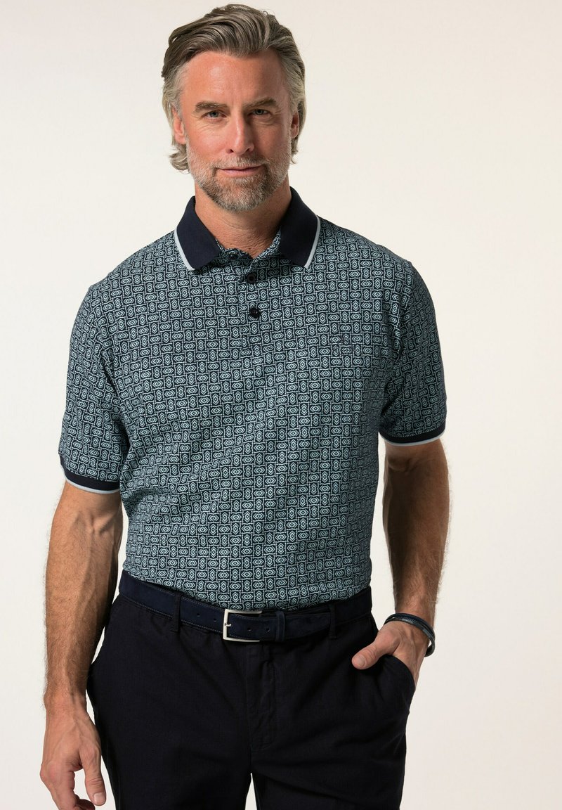 Pánská polokošile s krátkým rukávem v námořnické modři s geometrickým vzorem, bílými akcenty na límci a volným střihem, ve spojení s tmavými kalhotami.