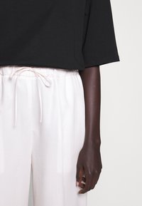 Svart kortärmad topp i kombination med ljusrosa, löst sittande byxor med dragsko i midjan. Slätt tyg med en svag lysty.