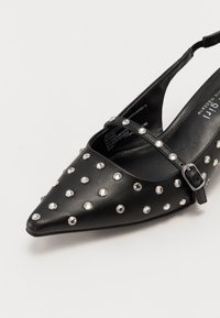Chaussure plate slingback noire à bout pointu avec ornements en clous argentés et bride à boucle réglable.