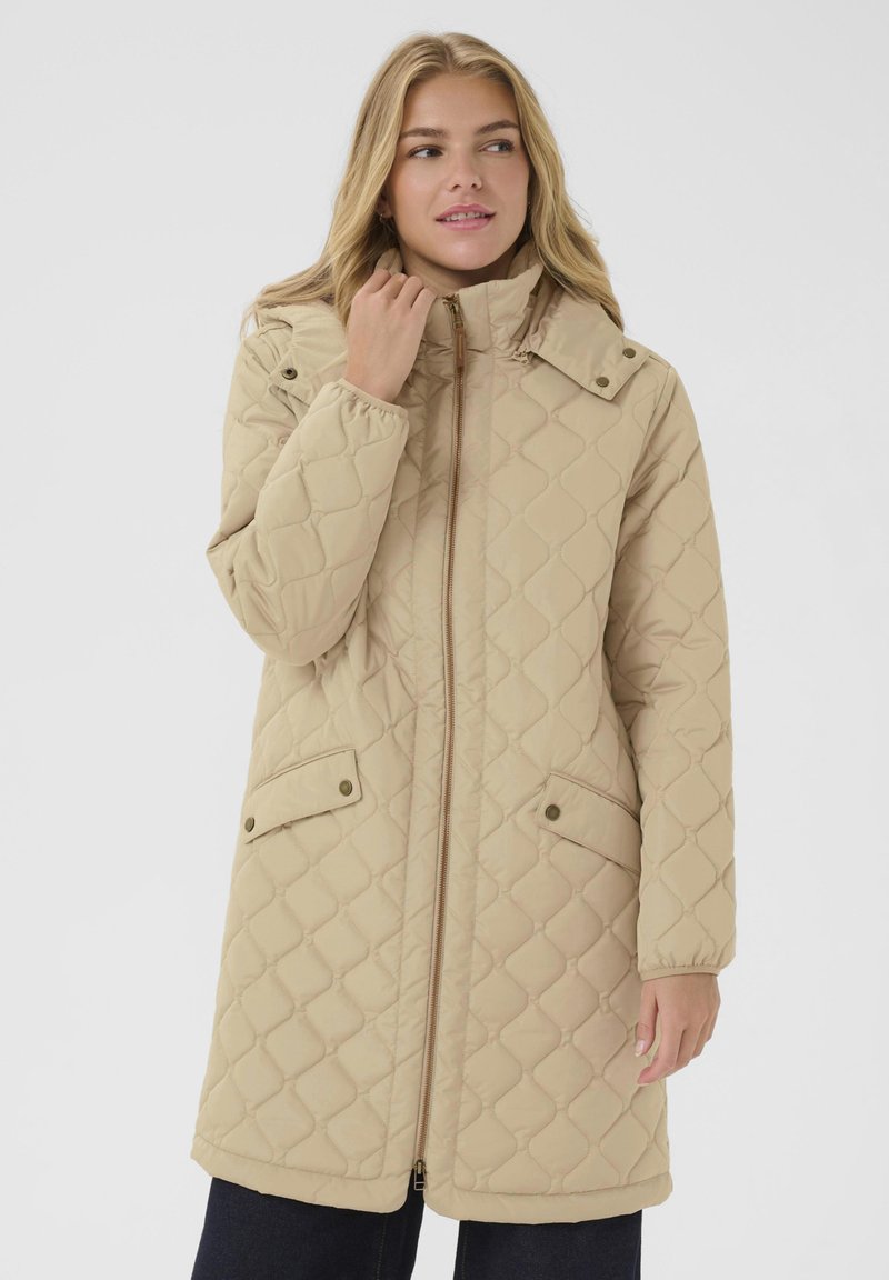 Beige quiltad långjacka med hög krage, sidofickor, framzipper och tryckknappar. Mjuk, slitstark tyg med en något glänsande yta.