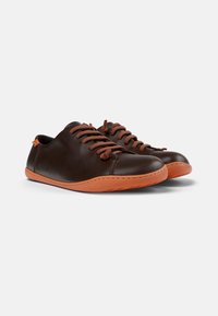 Zapatos de cuero marrón con suelas de goma naranja, con cordones y costuras marrones, punta redondeada y un diseño minimalista.