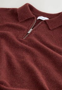 Burgundijas krāsas puloveris ar rāvējslēdzēju, izgatavots no maigas, teksturētas auduma. Iespējas: apkakle un sudraba rāvējslēdzēja detaļa priekšā. Etiķete redzama iekšpusē.