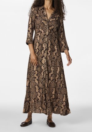 Pitkähihainen mekko, jossa on ruskea ja beige käärmekuvio, etupuolella napillinen ja väljä siluetti, yhdistetty tummiin tasapohjaisiin kenkiin.