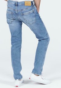 Jasnoniebieskie dżinsy ze slim fit, z dwiema tylnymi kieszeniami i brązową metką marki na pasku. Noszone z białymi trampkami.