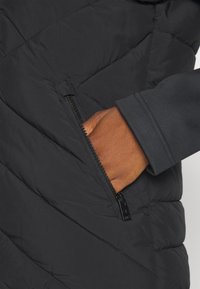 Czarna pikowana kurtka z przeszyciami, kieszenią na suwak po boku i gładką fakturą materiału na rękawie.