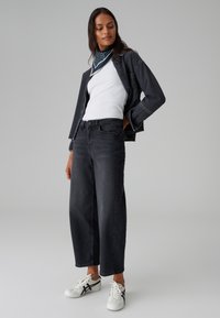 Jeans neri a gamba larga con vita alta, abbinati a una canottiera bianca e a una giacca di denim scuro. Include sneakers bianche con dettagli neri.