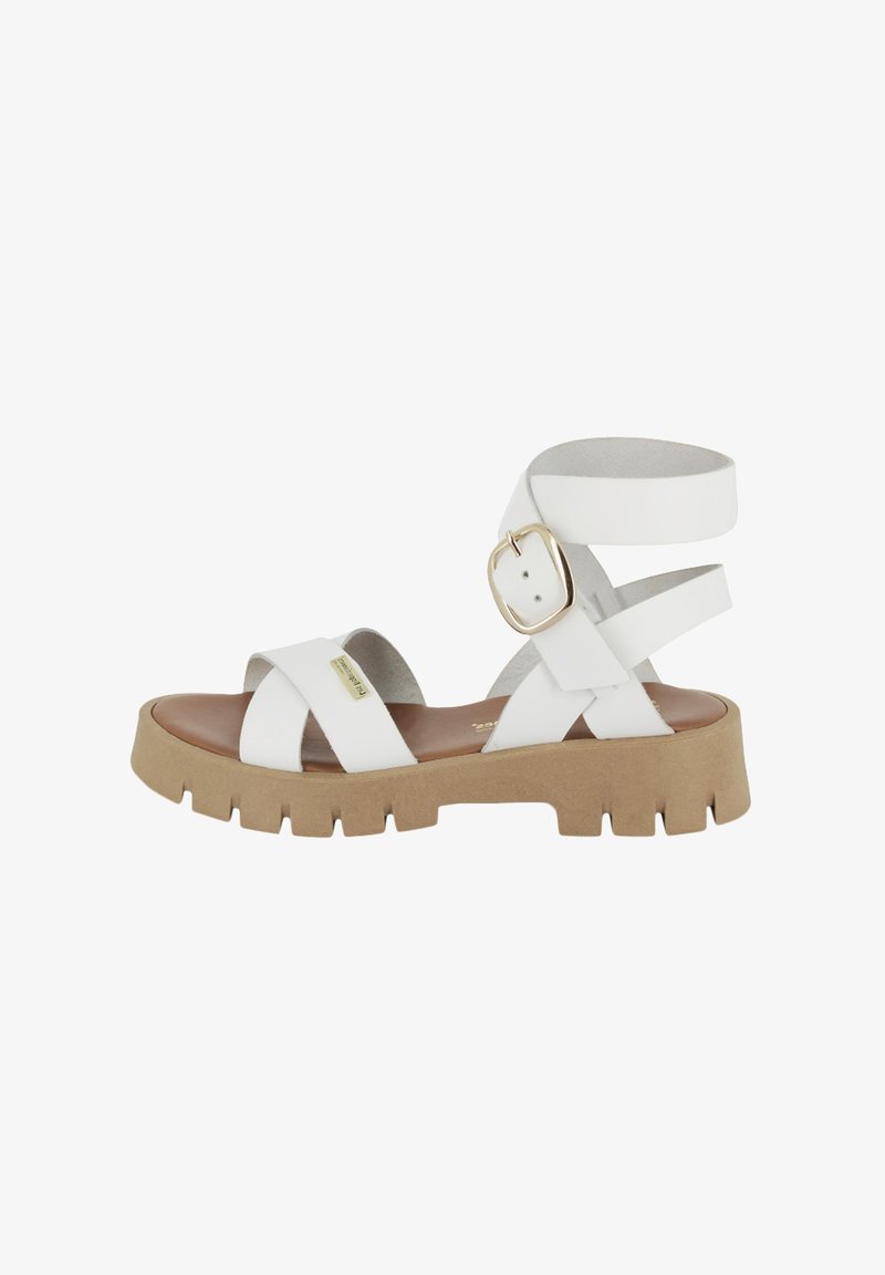 Sandal in pelle bianca con accentuazione a fibbia, cinturini incrociati e una suola spessa in gomma marrone con un motivo rigato per una presa migliore.