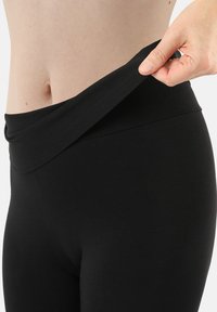 Black leggings with a wide, folded waistband, made from stretchy material. Close-up view shows smooth texture and fitted design.