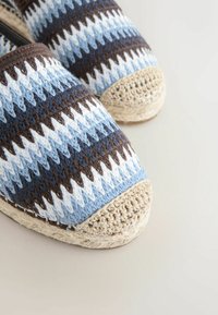 Primo piano di scarpe espadrillas tessute con motivi a zigzag in tonalità di blu, bianco e marrone con punta e suola beige intrecciata.