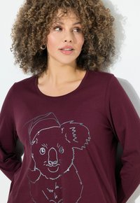 Bordeaux lange mouwen shirt met een zilveren omlijning van een koala die een hoed draagt. Zacht, katoenmateriaal met een ronde halslijn en een relaxte pasvorm.