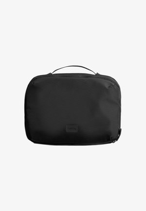 Organisateur de voyage rectangulaire en nylon noir, avec une poignée supérieure, une fermeture éclair et un logo discrètement embossé à l'avant.