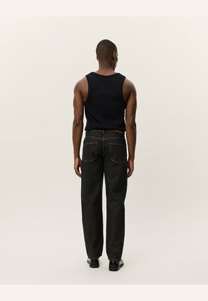 Camiseta sin mangas negra combinada con jeans de mezclilla oscuros que cuentan con bolsillos traseros, costuras visibles y piernas ligeramente entalladas en un acabado texturizado.