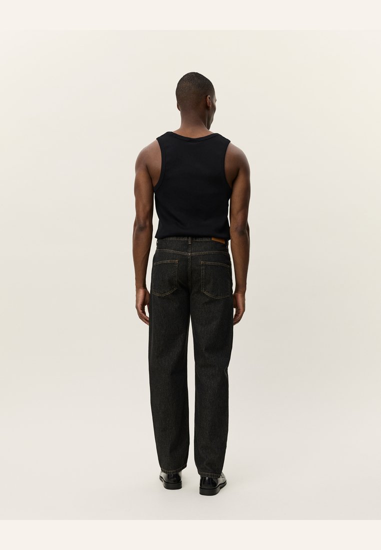 Black sleeveless tank top paired with dark denim jeans featuring back pockets, visible stitching, and slightly tapered legs in a textured finish.
