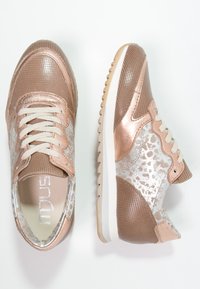 Tenisky se síťovaným designem v světlé béžové barvě s kovovými akcenty, texturovanými povrchy a kontrastní bílou podrážkou.