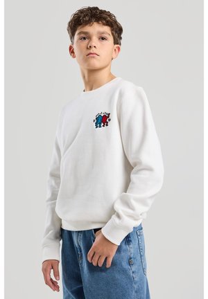 Witte sweatshirt met lange mouwen, voorzien van een kleurrijk geborduurd ontwerp van blauwe en rode figuren op de borst. Gecombineerd met lichtblauwe denim jeans.