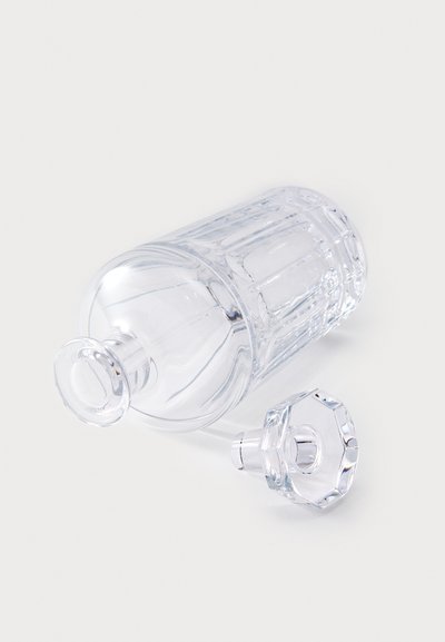 Contenedor de vidrio transparente con cuerpo cilíndrico y tapa plana. Presenta líneas verticales y una abertura redonda en la parte superior. La tapa tiene forma octogonal.