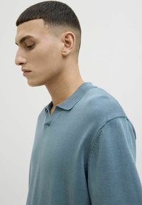 Polo en tricot bleu clair avec un col moyen, des manches courtes et une coupe décontractée ; tissu texturé avec des détails de couture visibles.