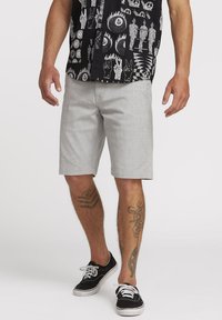 Light gray shorts in a relaxed fit, made from a smooth fabric, with side pockets and rolled hems, paired with a patterned black shirt.